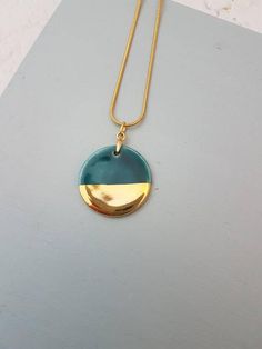 a gold and teal necklace on a gray surface with a white marble table in the background