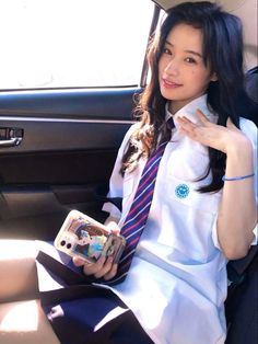 a woman sitting in the back seat of a car holding a cell phone and wearing a tie