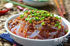 a white bowl filled with red onions and green onions next to chopsticks on a table