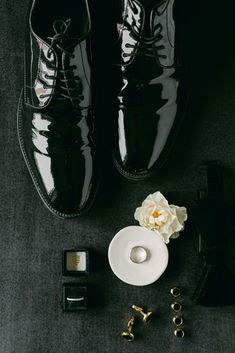 a pair of black shoes next to a white flower and other accessories on a gray surface