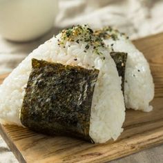 two pieces of sushi sitting on top of a wooden cutting board next to a glass of milk