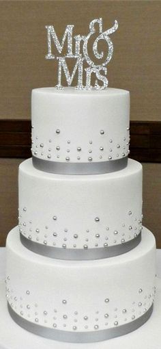 a three tiered white cake with silver ribbon and mr and mrs letters on top