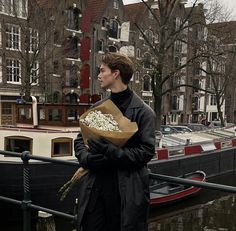 a man holding flowers standing next to a boat