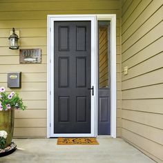 a black front door on a house with flowers in the planter next to it