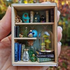 someone is holding a miniature book shelf with books and figurines on it in their hand