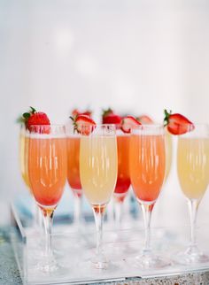 four glasses filled with champagne and strawberries sit on a tray, ready to be served