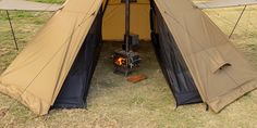 a tent set up in the middle of a field with an open fire place next to it