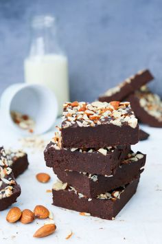 some brownies are stacked on top of each other with nuts and milk in the background