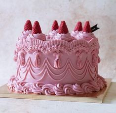 a cake with pink frosting and strawberries on top is sitting on a wooden board