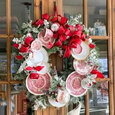 a christmas wreath with red bows and plates hanging on the front door, next to an old china cabinet