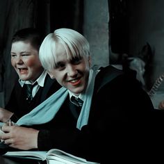 two young boys dressed in harry potter costumes sitting at a table with an open book