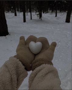 two hands in mittens holding a white heart shaped object with trees in the background