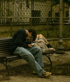 a man and woman sitting on a bench in front of a fence, one kissing the other