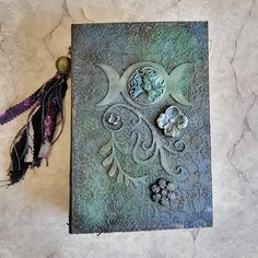 a book with an intricate design and tassels on the cover sitting on a table