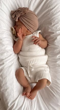 a baby laying on top of a bed wearing a white outfit and a headband