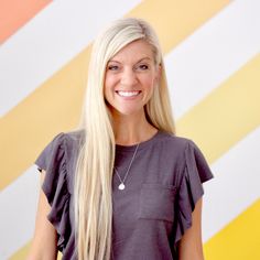 a woman with long blonde hair standing in front of a colorful wall and smiling at the camera