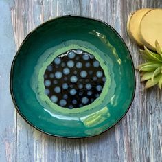 a green bowl filled with black dots on top of a wooden table