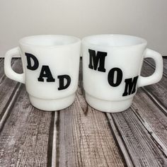 two white coffee mugs with the words dad and mom printed on them sitting side by side