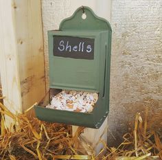 a green mailbox with the word sheila written on it in front of some dry grass