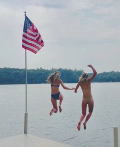 two girls jumping into the water with an american flag flying in the air behind them