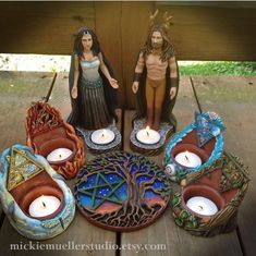 a couple of statues sitting on top of a table next to candles in bowls and vases