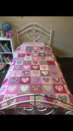 a bed with pink and white quilted hearts on the bedspread next to a bookcase