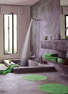 a bathroom with a tub, shower head and green rugs on the floor in front of two windows