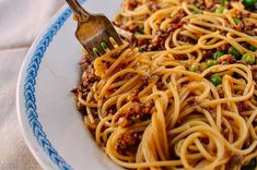 a close up of a plate of spaghetti with meat and peas on it, with a fork stuck in the pasta