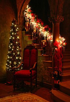 a red chair sitting in front of a christmas tree next to a stair case with lights on it