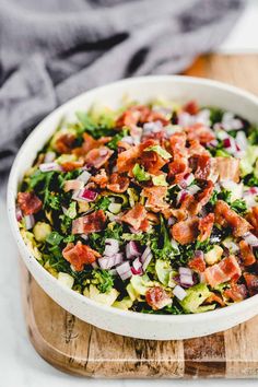 a white bowl filled with bacon, lettuce and onion salad on top of a wooden cutting board