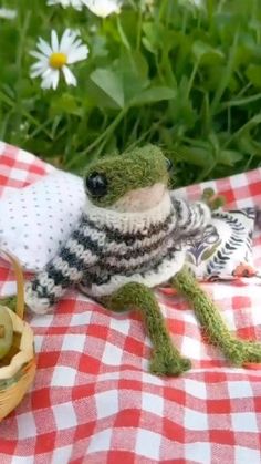 a stuffed frog sitting on top of a red and white checkered table cloth next to a basket