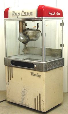 an old fashioned popcorn machine sitting on top of a cement floor next to a white wall