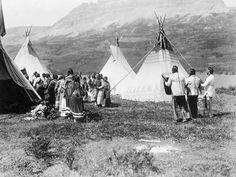 an old black and white photo of people standing in front of some teepees