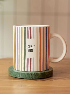 a coffee mug with the words cest bon on it sitting on a wooden table