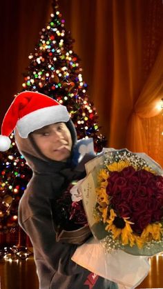 a woman in a santa hat holding a bouquet of sunflowers with a christmas tree behind her