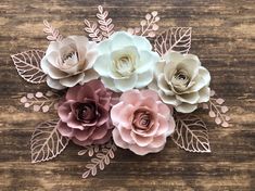 paper flowers are arranged on a wooden surface, with leaves and branches in the center