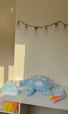 a stuffed alligator is sitting on a shelf in front of a wall with christmas lights