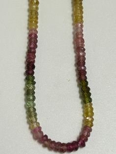 multicolored glass beads are on a white surface and one bead is hanging from the end