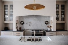 a kitchen with white cabinets and marble counter tops, an island style sink and two faucets