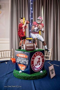 two football players are posed on top of a trophy at a sports themed event with lights in the background