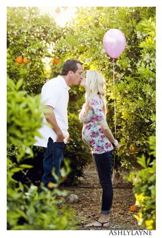 a man and woman kissing in an orange grove with pink balloons attached to the strings