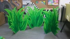 some green plants and zebras are on the table in front of a cardboard board