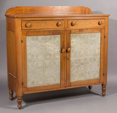 an old wooden cabinet with carved designs on the doors and drawer handles, is shown against a gray background