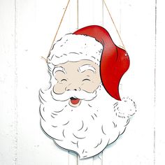 a paper cut out of santa claus hanging on a white wooden wall with a red hat