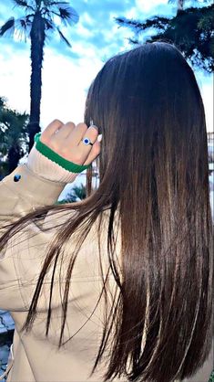 a woman with long brown hair is talking on her cell phone while standing in front of palm trees