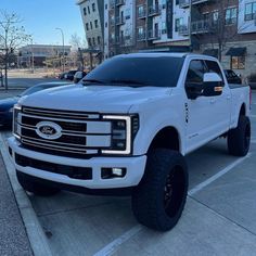 a white pickup truck parked in a parking lot next to some tall buildings and cars