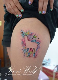 a woman's thigh with an unicorn tattoo on the side and colorful paint splatters all over it