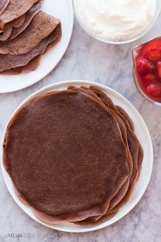 two plates with pancakes, strawberries and whipped cream on them next to bowls of fruit