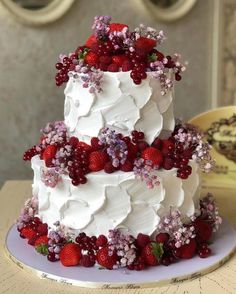 a three tiered cake with white frosting and fresh berries on the top, sitting on a table