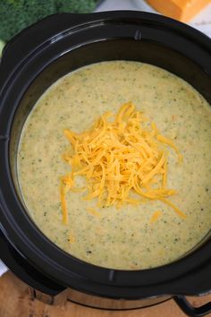 a black crock pot filled with cheese and broccoli on top of a table